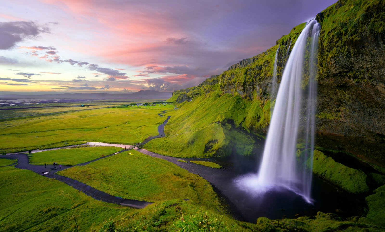 therapie-breve-falaise-cascade-vitalite-emotionnelle-collaure.com Photo d'un paysage apaisant avec une cascade qui surplombe une vallée de végétation sous le soleil couchant, propice au ressourcement via la Vitalité Émotionnelle de Laure Colla. collaure.com
