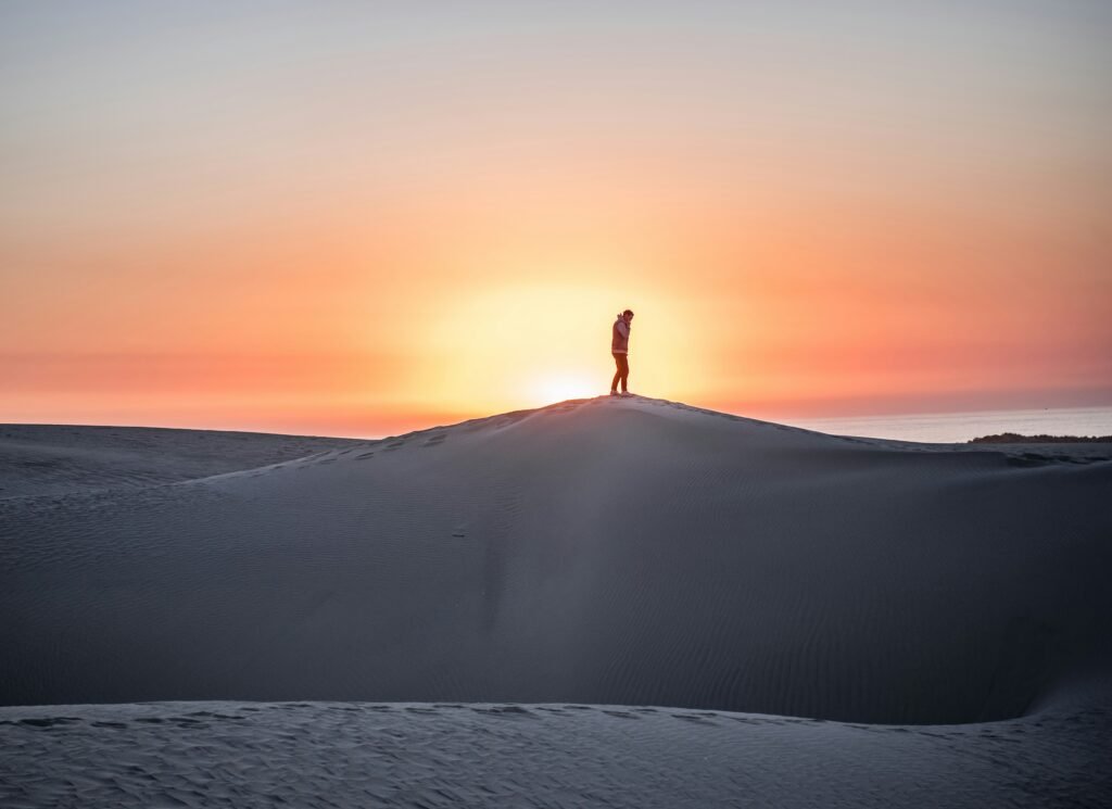Un homme qui marche seul en haut d'une montagne au soleil couchant, en introspection, réalisant peut-être sa tendance à l'autosabotage. Blog Laure Colla Vitalité Émotionnelle.